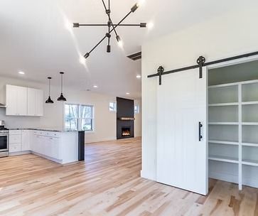 Bright open kitchen and dining area with white cabinets, wood floors, and a sliding barn door to a closet.