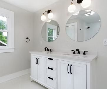 Bright modern bathroom vanity with double sinks, round mirrors, and wall sconces