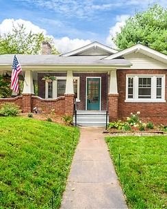 Brick house with a front porch, American flag, and a walkway through a green lawn.