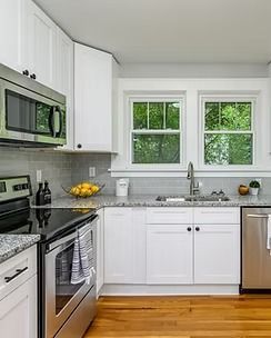 Bright white kitchen with stainless steel appliances, window above sink, and hardwood floors