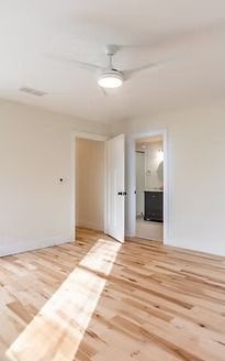 Empty white bedroom with hardwood floors, ceiling fan, and open door to adjoining room.