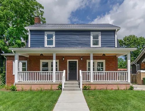 Blue-and-brick two-story house with a front porch, white railings, and a centered walkway
