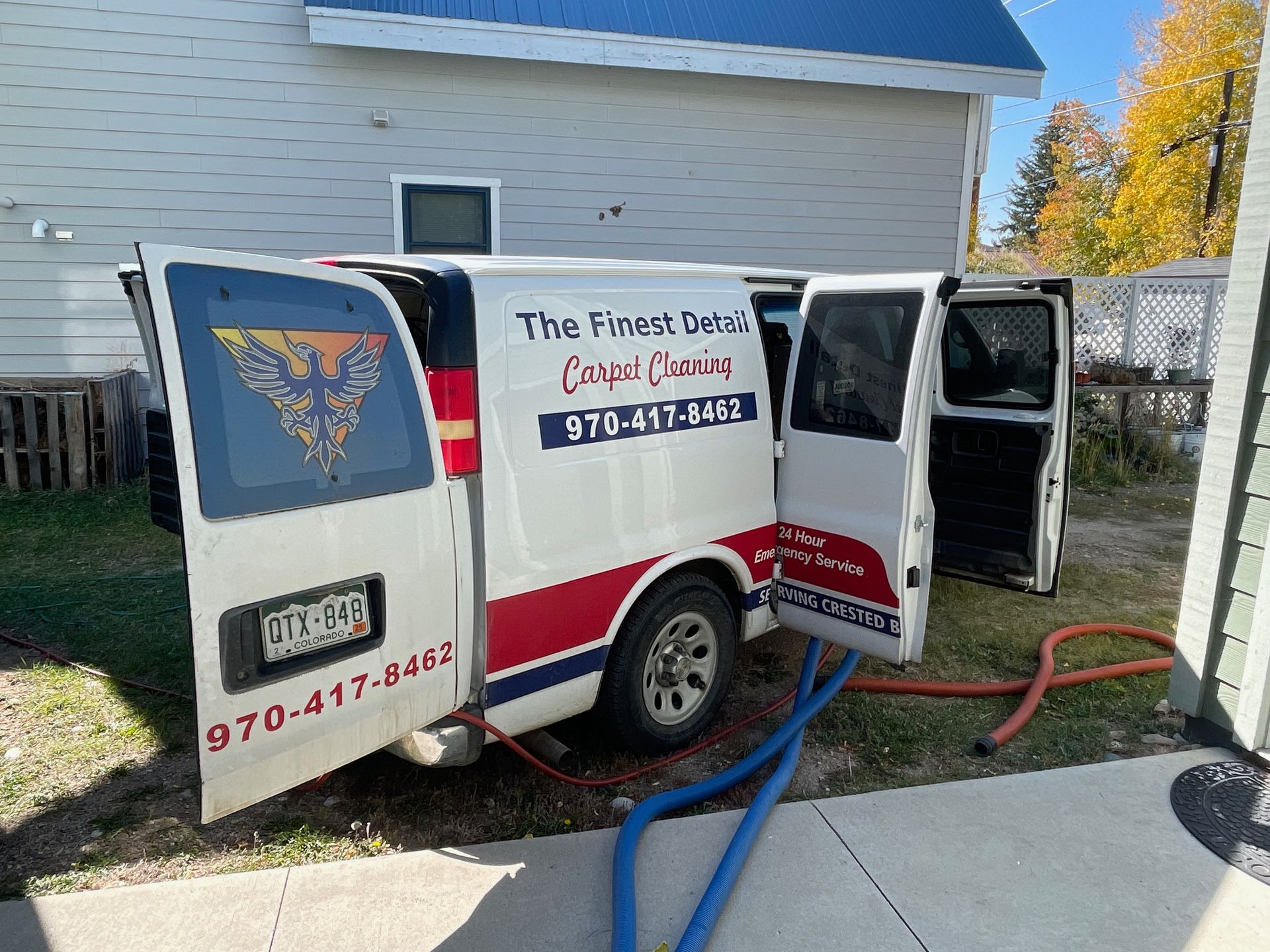 A white van with the doors open is parked in front of a house.