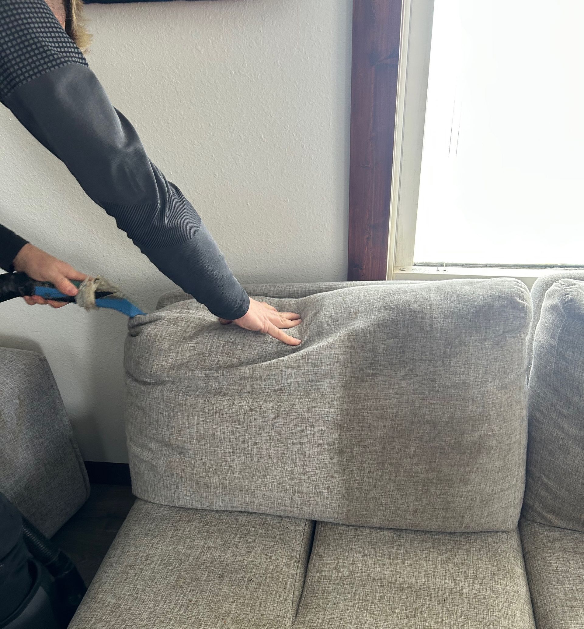 A person is cleaning a couch with a vacuum cleaner.