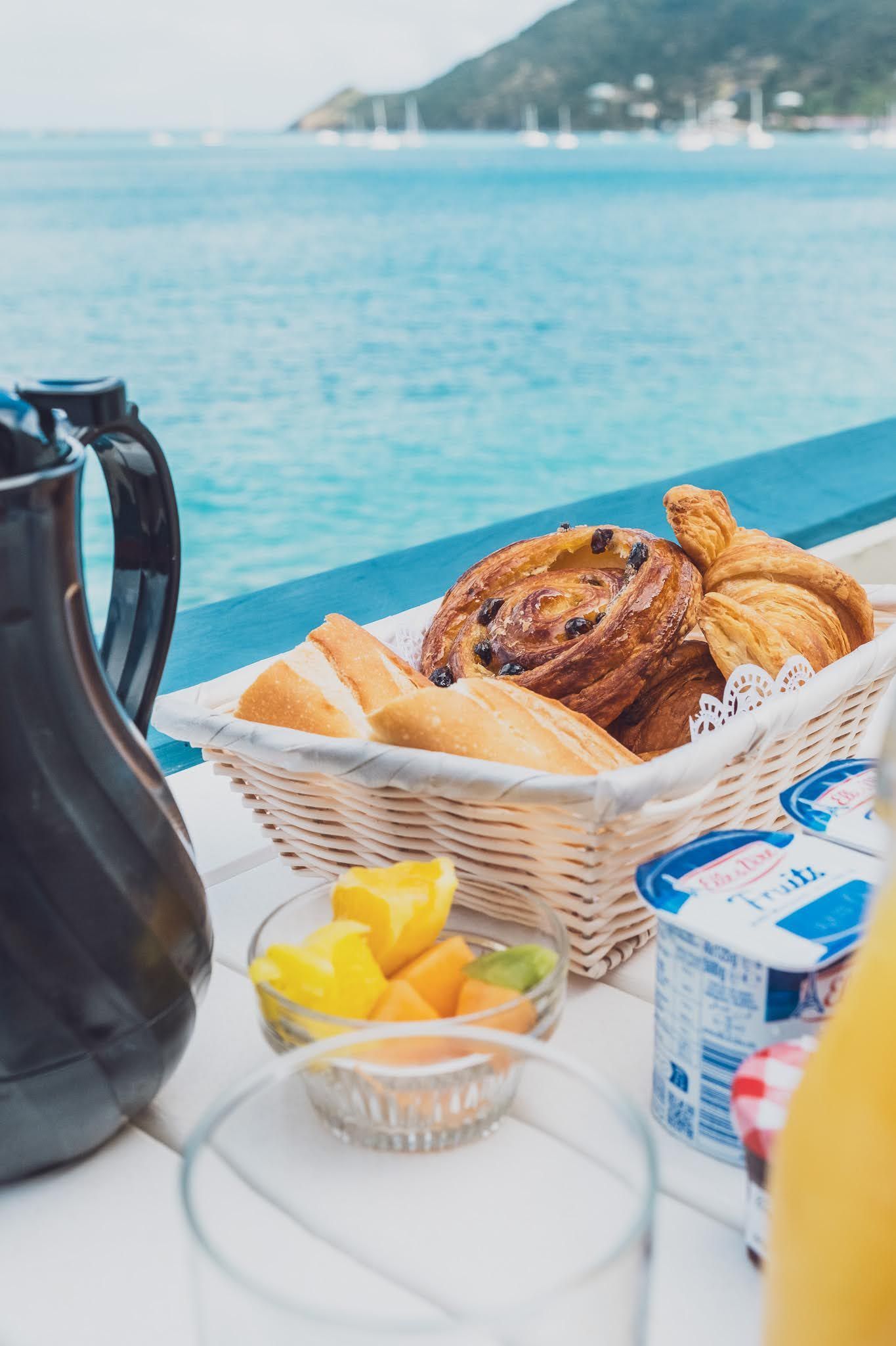 Breakfast spread by the ocean with bread, fruit, yogurt, and a carafe.