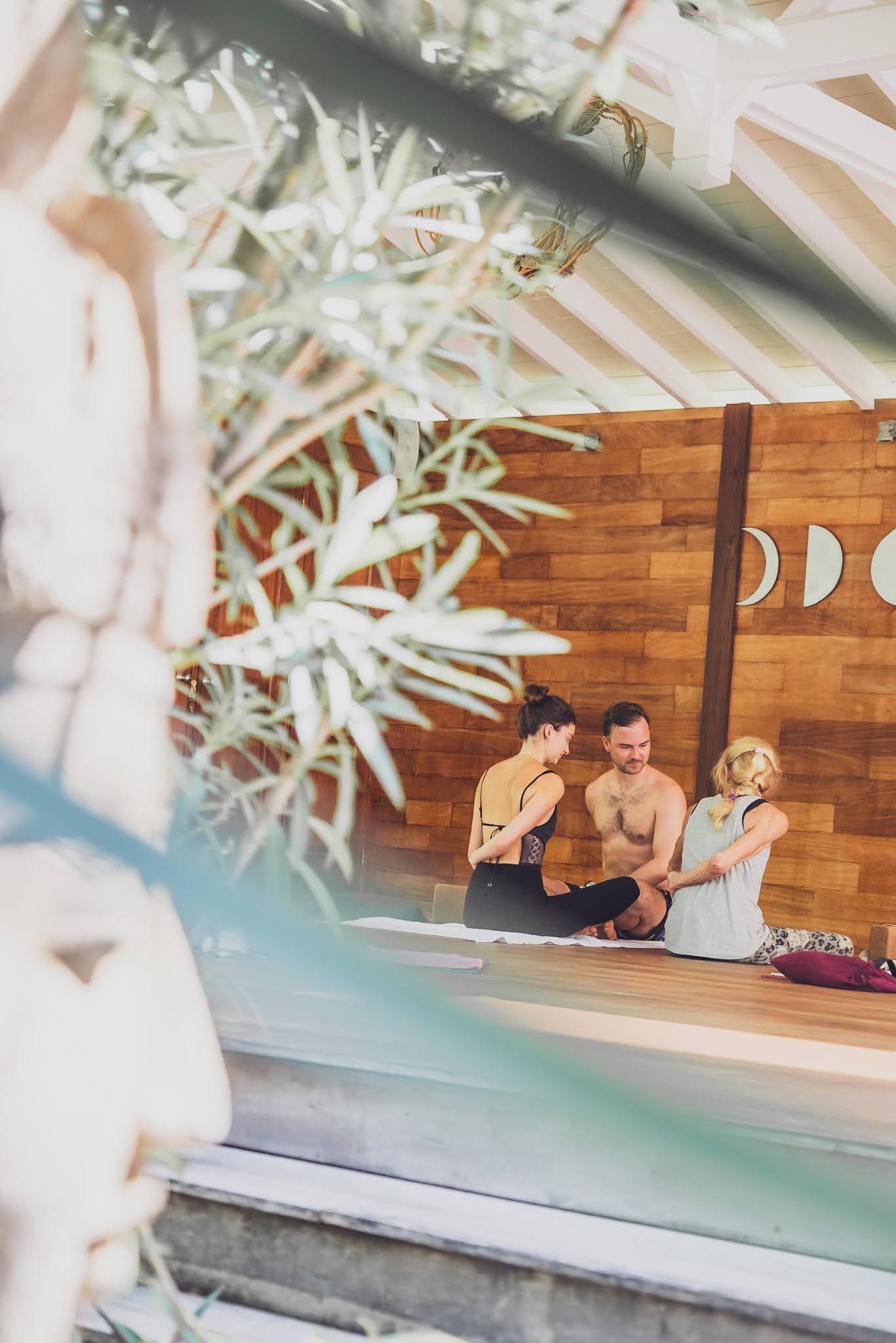 People seated in a yoga studio, wood walls, moon decor. Focus is on wellness and meditation.
