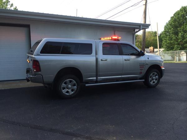 Silver pickup truck with a cap and emergency lights parked in front of a building.