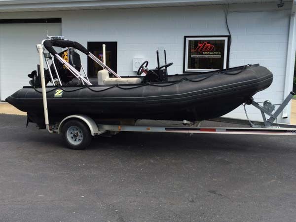 Black rigid inflatable boat on a trailer, parked on a paved surface next to a building.