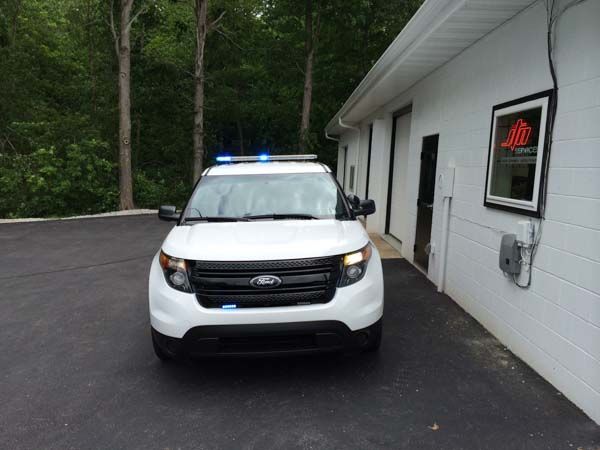 White police SUV with blue lights parked outside a building with trees in the background.