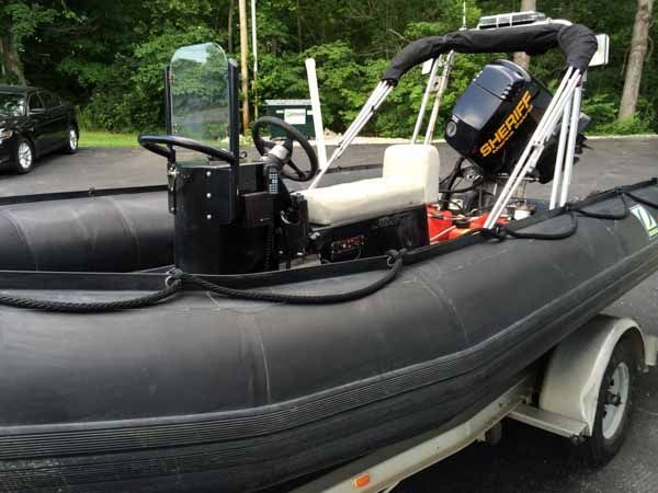 Black inflatable boat on a trailer, with outboard motor and steering console.