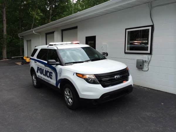White police SUV parked outside a white building. Blue POLICE lettering and light bar visible.