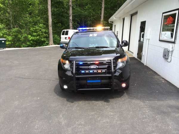Black police SUV with emergency lights parked next to a white building.
