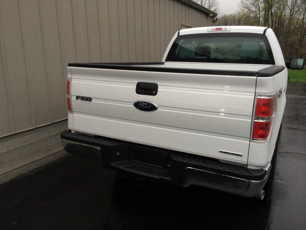 White Ford F-150 truck, rear view, parked on pavement next to a building.