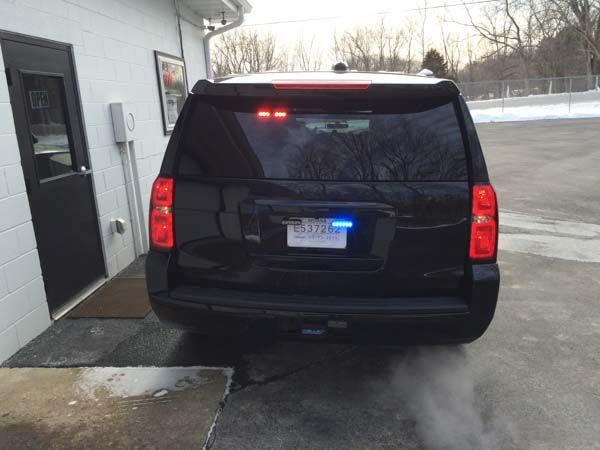 Black SUV with flashing lights parked outside a building, exhaust visible.