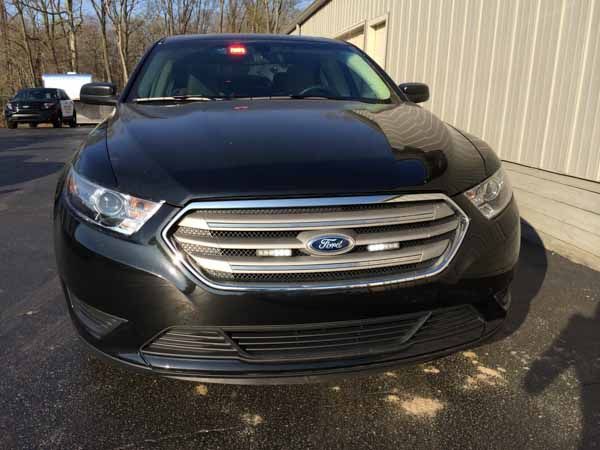 Black Ford Taurus police car with flashing red lights, parked in front of a building.