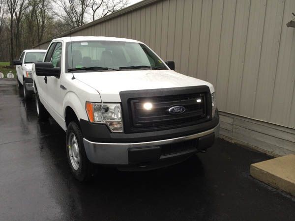 White Ford F-150 truck parked next to a building. The truck has a black grill and bumper. Rainy day.