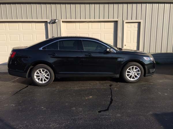 Black Ford Taurus parked in front of tan storage units.