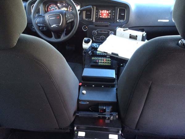 Interior view of a police car with center console equipment, steering wheel, and dashboard.