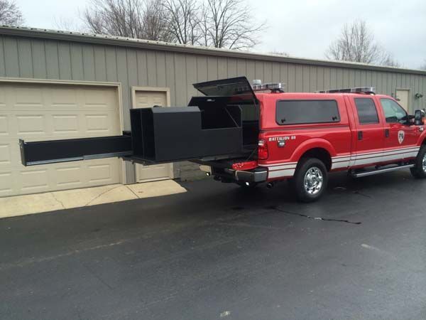 Red fire truck with a black, extendable storage compartment pulled out, parked in front of a building.