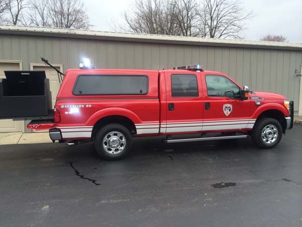 Red Ford F-350 fire department truck with canopy parked in front of a building.