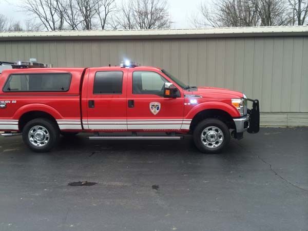 Red emergency pickup truck with white stripe, lights, and canopy parked outside building.