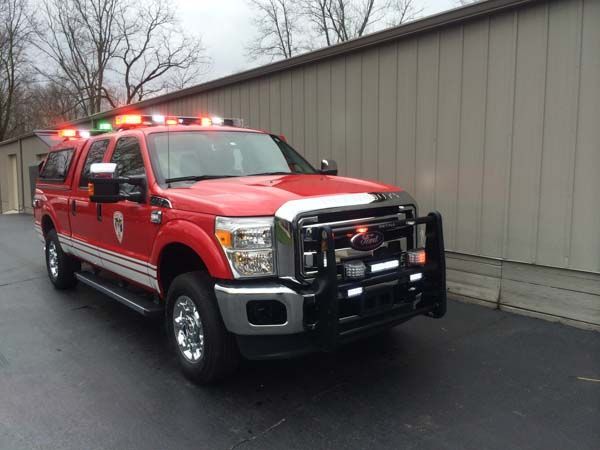 Red fire service truck with flashing lights parked in front of a tan building.