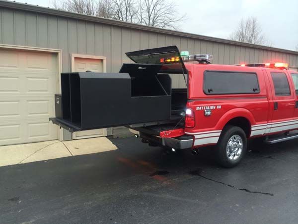 Red fire truck with open rear storage compartment and emergency lights on.