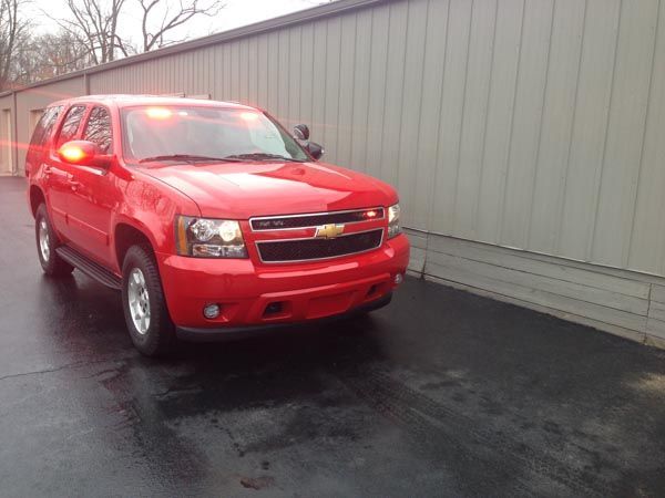 Red SUV with flashing lights parked next to a light-colored building.