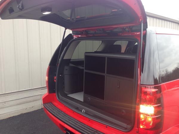 Red SUV trunk open, revealing a black cabinet with drawers and shelves. Interior view.