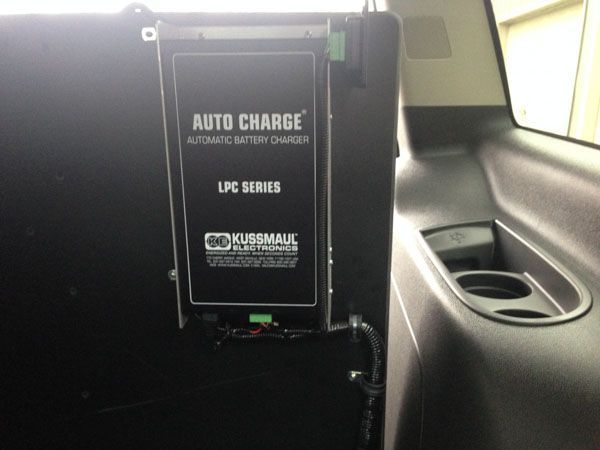 Black Auto Charge battery charger installed in a vehicle, next to a cup holder.