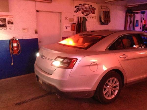 Silver car inside a garage; taillights illuminated. A fire extinguisher is mounted on the wall.