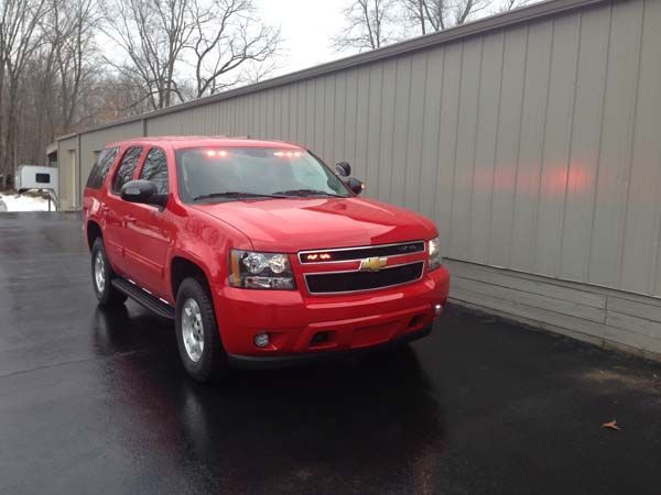 Red SUV with emergency lights parked next to a gray building.