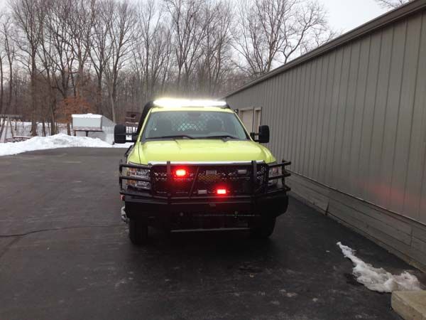 Yellow pickup truck with emergency lights on, parked outside a building in winter.
