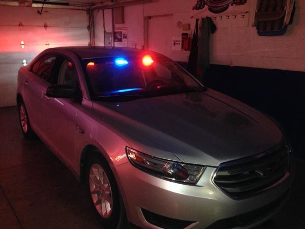 Silver car with red and blue emergency lights in a garage.