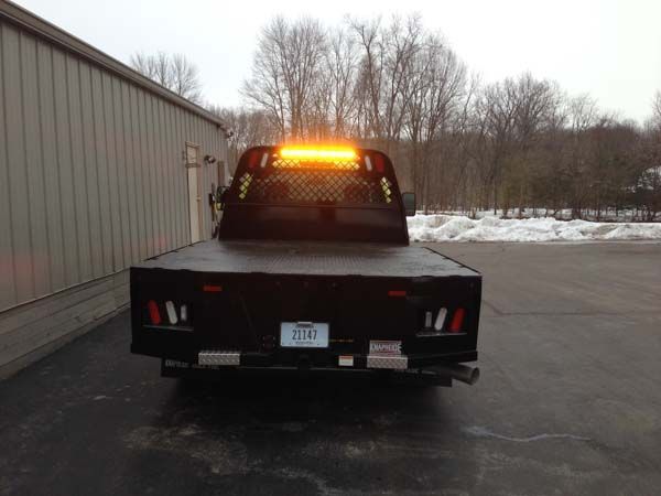 Black flatbed truck with amber light on roof, parked in front of a building, snow in the background.
