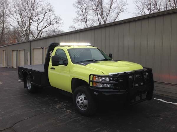 Yellow and black flatbed truck parked in front of a gray building, under an overcast sky.