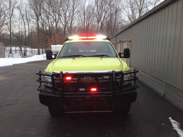 Yellow emergency vehicle with flashing red and white lights, parked in front of a building with snowy ground.