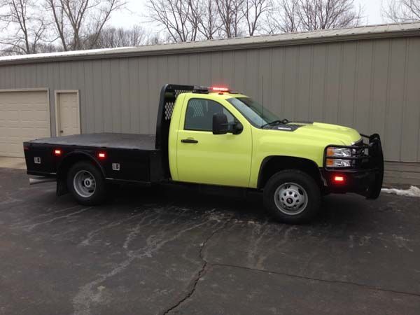 Yellow and black flatbed truck with emergency lights parked in front of a building.