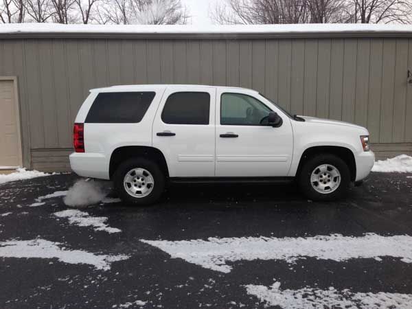 White SUV parked in front of a gray building. Snow on the ground.