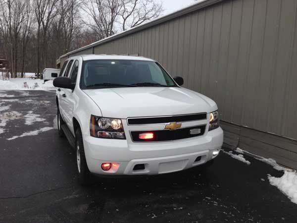White SUV with emergency lights parked in front of a building with snow on the ground.