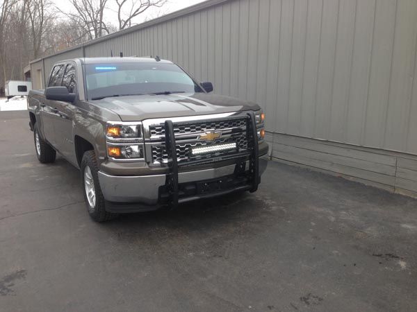 Gray Chevy pickup truck with brush guard, parked on asphalt by a gray building.