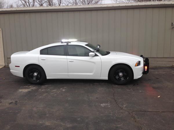 White police car with black wheels and push bar parked outside a building.