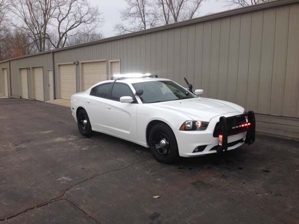 White police car parked near a building with garage doors. It has emergency lights and a front push bar.
