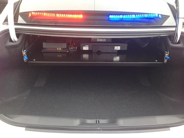 Open trunk of police car with shelf holding electronic equipment; red/blue light bar visible above.