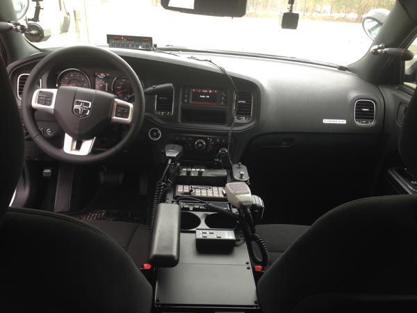 Interior of a police Dodge Charger patrol car, black dashboard with steering wheel, center console, and radio equipment.