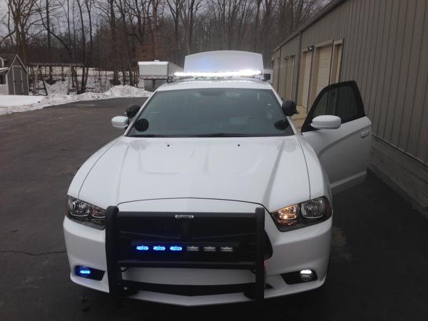 White police car with emergency lights on, parked outside a building, door open.