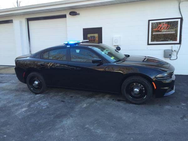 Black police car with flashing blue lights parked outside a building.
