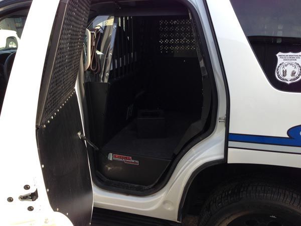 Inside of a police vehicle with a partition between the front and back seats, back door open.