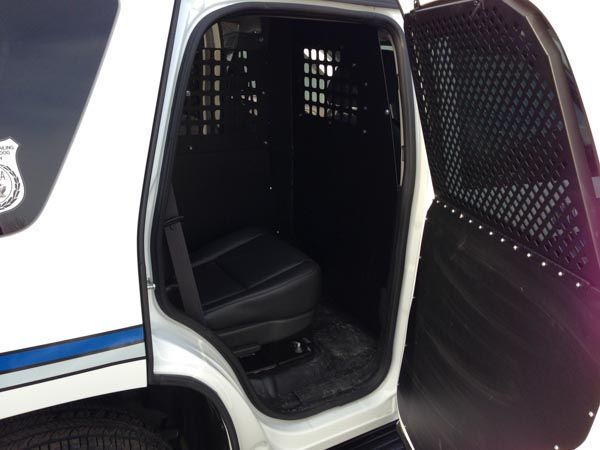 Interior of a police vehicle with a black prisoner transport area and a grated door.
