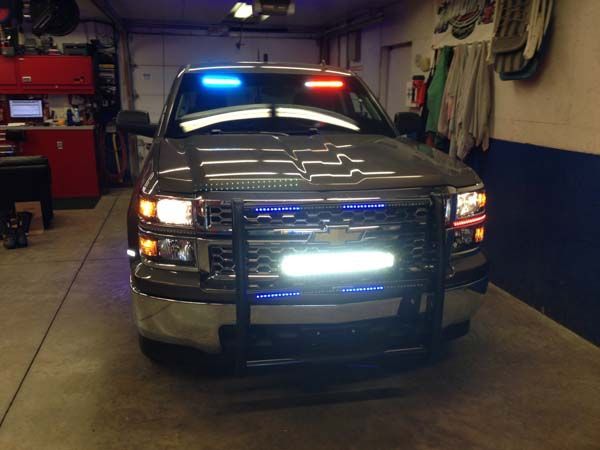 Silver truck with emergency lights flashing blue and red, parked in a garage.